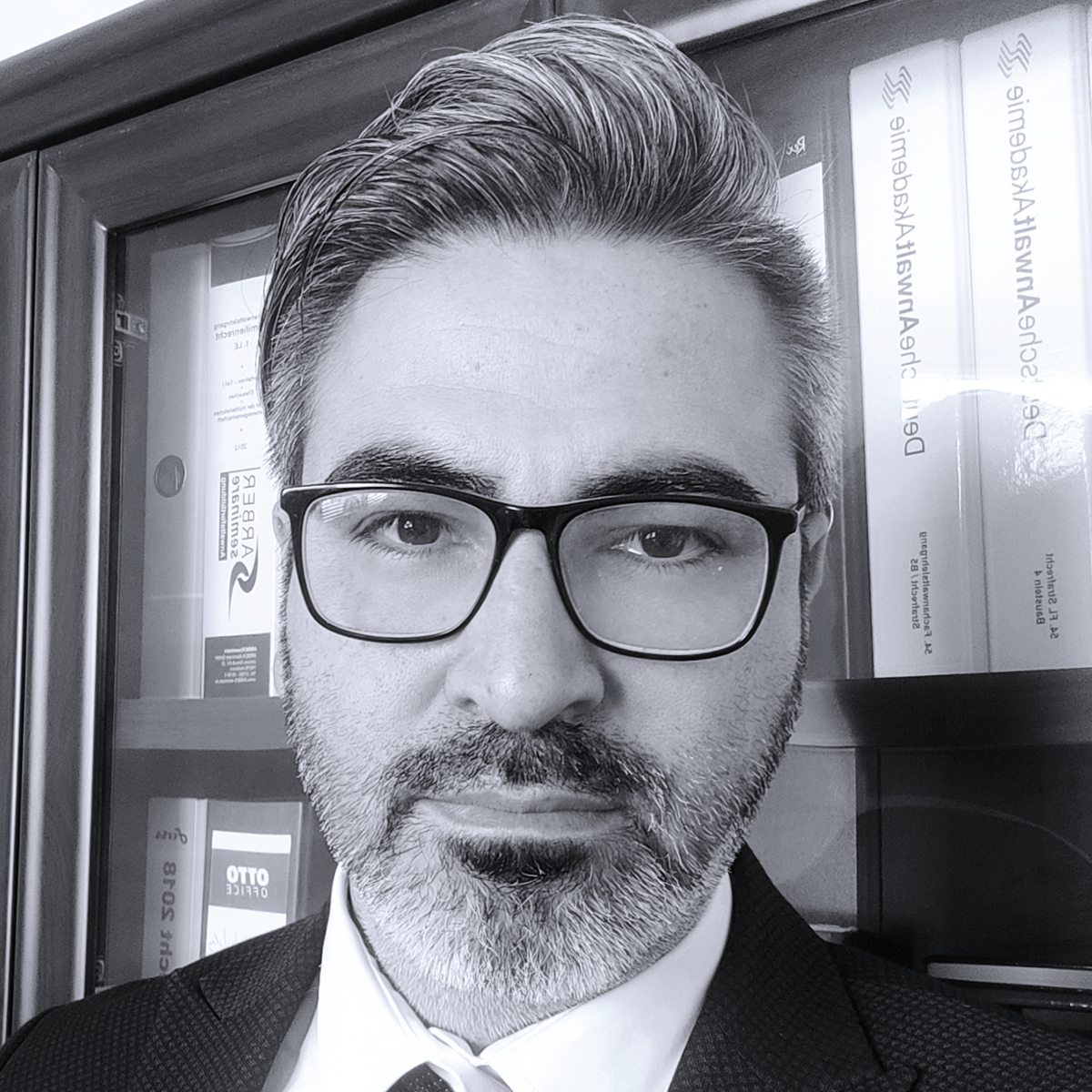 Rechtsanwalt Önder Bogazkaya, Schwarz-Weiß-Porträt mit Brille vor einem Bücherregal